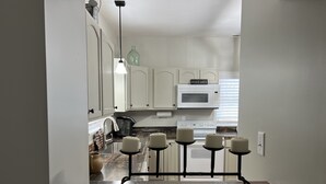 Une cuisine avec des meubles blancs, un four à micro-ondes, une cuisinière et un coin bar avec des tabourets.