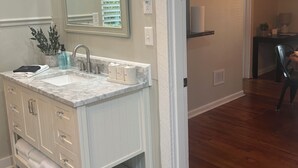Une salle de bain avec un meuble-lavabo blanc, un grand miroir, un évier avec un robinet et un porte-serviettes.