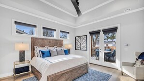 A bedroom with a large bed, a nightstand, a chair, and a view of the outdoors through a sliding door. - Lux 5BD Stonefront Tulsa | Near Gathering Place (Tulsa)