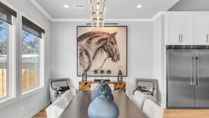 A modern kitchen with a large refrigerator, a dining table with chairs, and a large horse-themed painting on the wall. - Lux 5BD Stonefront Tulsa | Near Gathering Place (Tulsa)