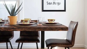 A dining area with a wooden table, two chairs, a bench, and a framed map of San Diego on the wall.