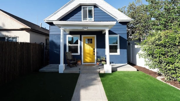 A two-story house with a blue exterior and a yellow front door, number 2964, with a small porch and a well-maintained lawn.