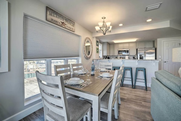 A dining area with a wooden table set for four, white chairs, and a view of the outside. - Steps to Beach + Gulf Views - 2BR/2BA - No Hidden Fees - Sleeps 8 (Mexico Beach)