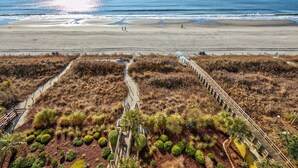 Eine Küstenlandschaft mit Strand, einer Promenade und einem Weg zu einer Holzkonstruktion.