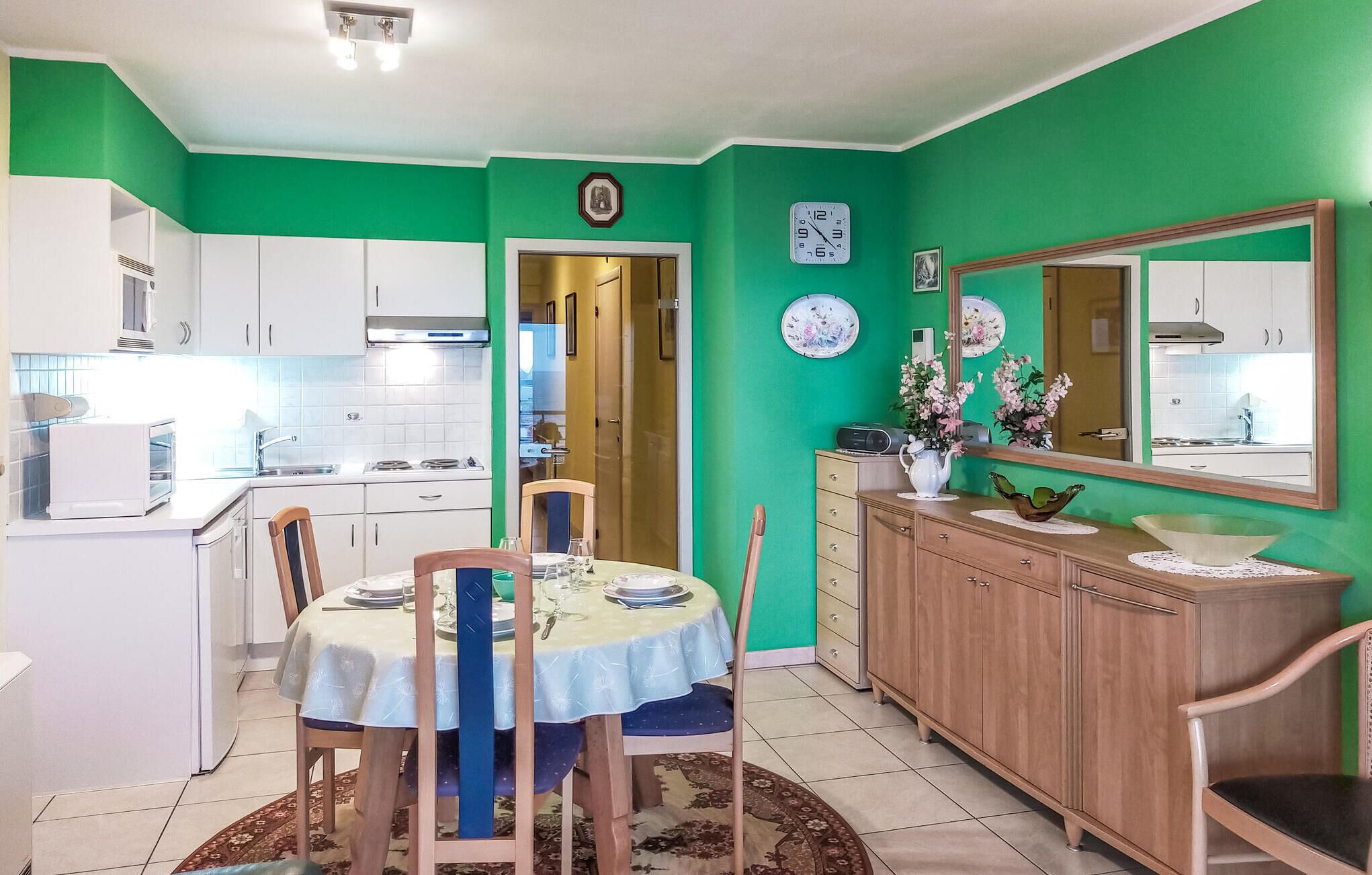 A compact kitchen with white cabinets, a dining area with a table set for two, and a green accent wall.