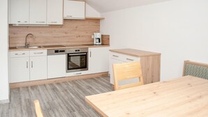 Una cocina compacta con armarios blancos, horno integrado, cafetera y una mesa de comedor de madera.