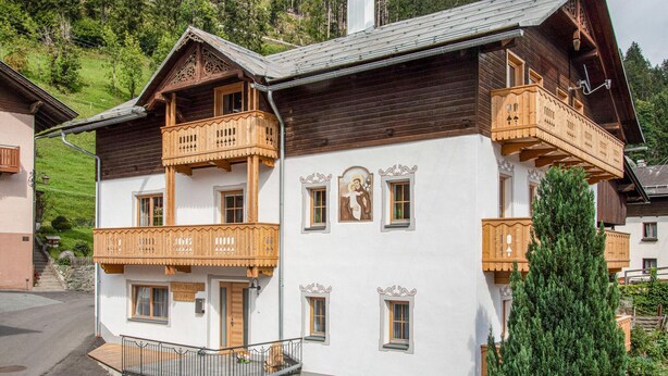 Un chalet de madera tradicional con balcones, una ventana central con un cuadro religioso, y una escalera que conduce a la entrada.