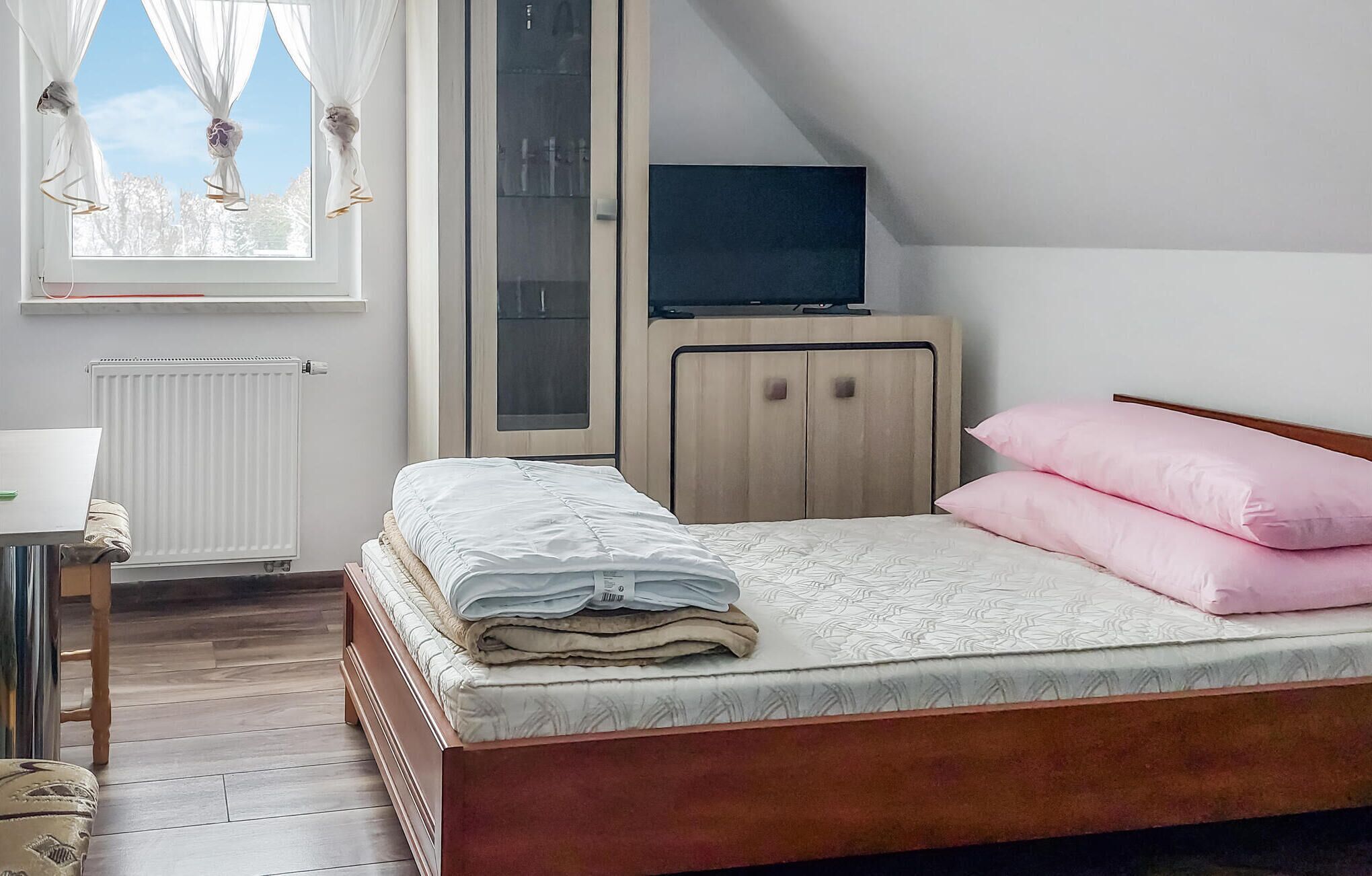 Un dormitorio con cama, televisor, armario y ventana con cortinas.