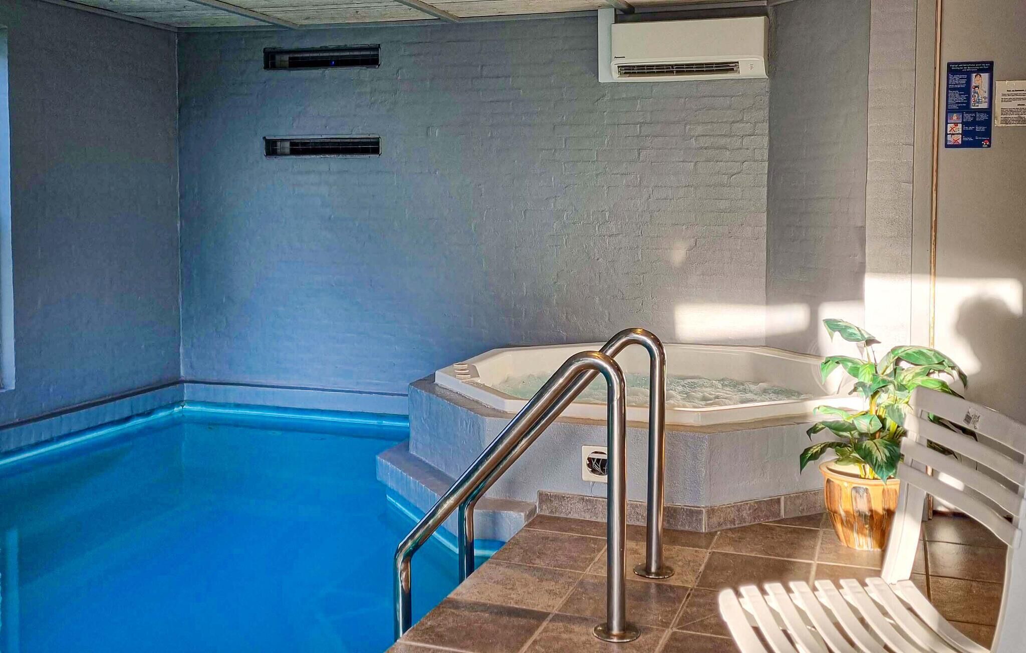 Piscina interna com hidromassagem, corrimão de metal e uma planta em vaso.