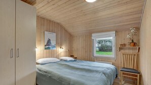 Een slaapkamer met een bed, een raam met uitzicht, een poster aan de muur en een plank met planten.