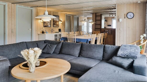 Een moderne woonkamer met een grijze modulaire bank, een houten salontafel en een eethoek op de achtergrond.