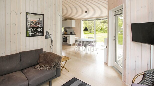 A modern interior with a sofa, dining table, and kitchen area, featuring wooden walls and large windows. - 2 bedroom awesome home in Samsø (Samsø)