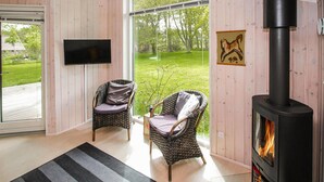 A cozy room with a fireplace, wicker chairs, a television, and a large window overlooking a garden. - 2 bedroom awesome home in Samsø (Samsø)