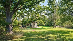A rustic cabin with a wooden exterior, surrounded by a lush green lawn and large trees. - 2 bedroom awesome home in Samsø (Samsø)