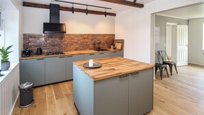 Eine moderne Küche mit einer zentralen Kochinsel, grauen Schränken, einer Ziegelrückwand und einer Holz Arbeitsplatte.