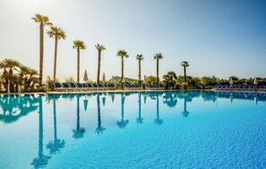 A clear blue pool with lounge chairs and palm trees.