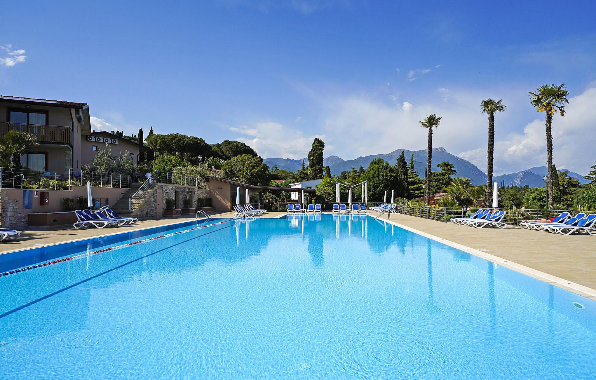 Une piscine avec des chaises longues, un escalier menant à un bâtiment et une vue sur les montagnes en arrière-plan.
