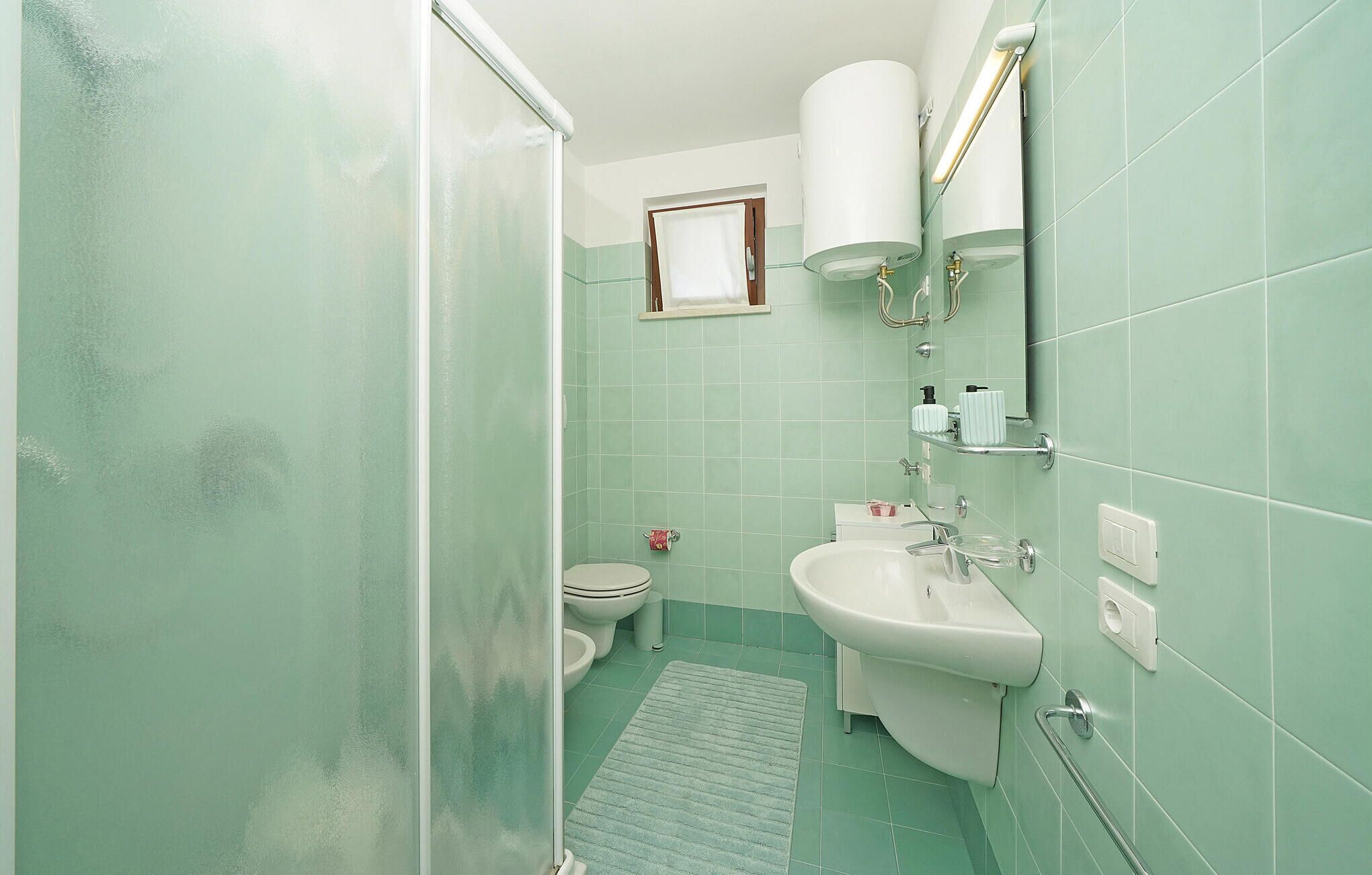 Een badkamer met een douche, toilet, wastafel en een klein raam.