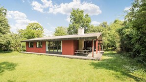 Een gelijkvloers huis met een overdekte veranda, een klein terras en een gazon.