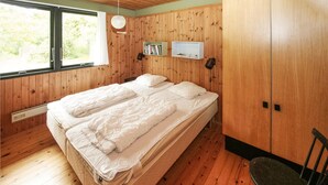 Een kamer met houten wanden en een bed met wit beddengoed. Er staat een stoel en een klein tafeltje.