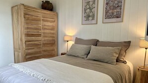 Un dormitorio con una cama, dos lámparas de pared, un armario de madera e ilustraciones botánicas enmarcadas.