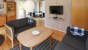 A living room with a sofa, a table, a TV mounted on the wall, and a wooden cabinet. - Nice home in Samsø with kitchen (Samsø)