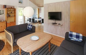 A living room with a sofa, a table, a TV mounted on the wall, and a wooden cabinet.