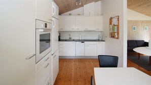 A compact kitchen with white cabinets, a built-in oven, and a coffee machine. There is a dining area with a white table and chairs. - Nice home in Samsø with kitchen (Samsø)