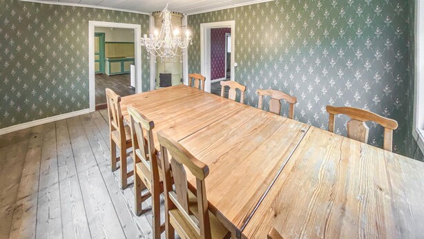 Un comedor con mesa y sillas de madera, una araña y papel tapiz estampado.