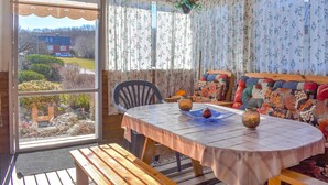 Una habitación acogedora con una mesa de madera, sillas y un banco. Una ventana con cortinas florales deja entrar luz natural.