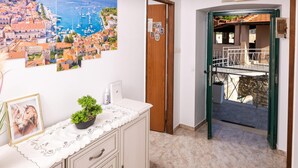 Een kamer met uitzicht op een kustplaatsje, een houten deur, een klein balkon met een metalen hekwerk en een plant op het aanrecht.
