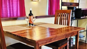 Een houten eettafel met stoelen, een fles wijn en glazen op een placemat.