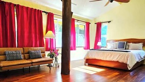 Een slaapkamer met een houten bed, een bank en rode gordijnen.