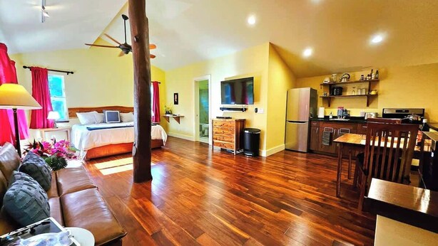 Een ruime woonkamer met houten vloer, een bank, een eettafel en een keuken met televisie.