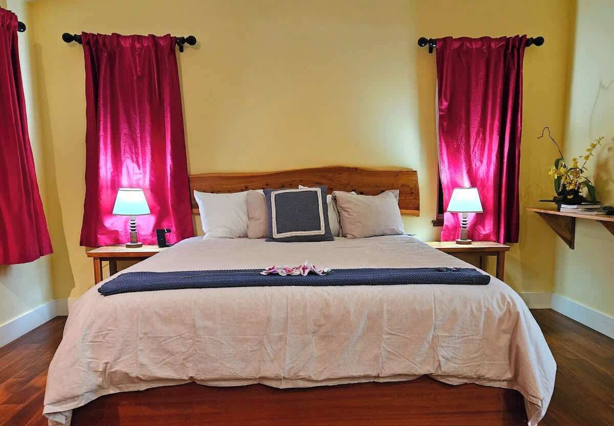 A neatly made bed with a wooden headboard, two bedside lamps, and a small table with a lamp and a vase of flowers.