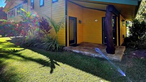 Een geel huis met een overdekte veranda en een kleine voortuin.