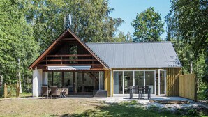 A cabin with a sloped roof, large windows, and a patio area with outdoor furniture. - Beautiful home in Samsø with WiFi (Samsø)