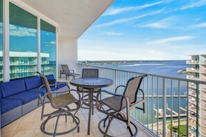 Un balcon avec vue sur l’eau, un canapé bleu, des fauteuils en osier et une table ronde.