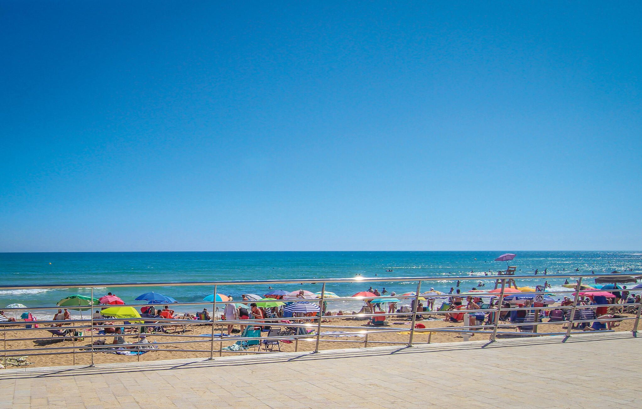 Una playa con cielo despejado, gente tomando el sol y sombrillas.