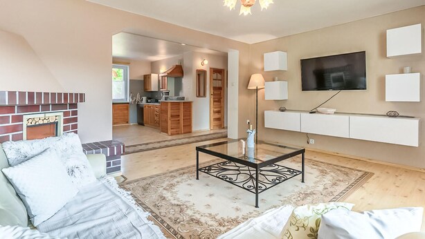 Una sala de estar con sofá, mesa de centro, chimenea, televisor montado en la pared y cocina al fondo.