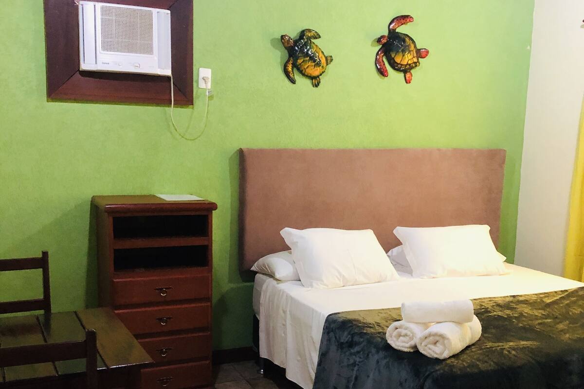 Une chambre à coucher comprenant un lit, une commode en bois, une chaise et un climatiseur fixé au mur.