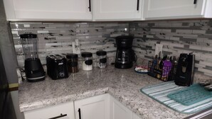 Een keuken met witte kastjes, een granieten aanrecht, een koffiezetapparaat, een blender en diverse keukengerei.