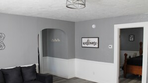 Een kamer met een donkergroene bank, een bed met een houten hoofdbord en een 'welcome' bord aan de muur.