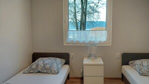 A bedroom with two beds, a nightstand, and a window with a view of trees.