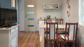 A compact kitchen with a built-in oven, a coffee maker, and a small refrigerator. There is a dining area with wooden chairs and a table.