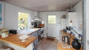 Eine kleine Küche mit Holzarbeitsplatten, einem Spülbecken, einem Herd und einem Kühlschrank. Hängelampen und ein Fenster sorgen für natürliches Licht.
