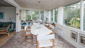 Eine geräumige Küche mit großem Esstisch, Holzstühlen und Blick auf den Garten durch große Fenster.