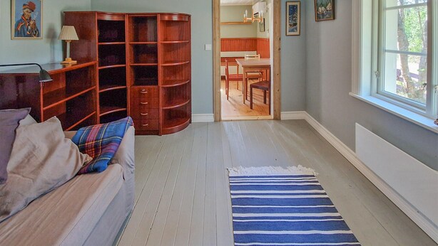 A room with a wooden floor, a striped rug, a wooden cabinet, a dining table with chairs, and a window with a view of trees. - 1 bedroom stunning home in Auktsjaur (Auktsjaur)