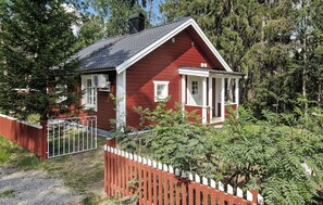 Une maison en bois rouge, avec un porche blanc, entourée de verdure.
