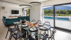 A modern dining area with a glass table and black chairs, overlooking a pool and mountains. - Pet friendly home in Radosic (Radosic)